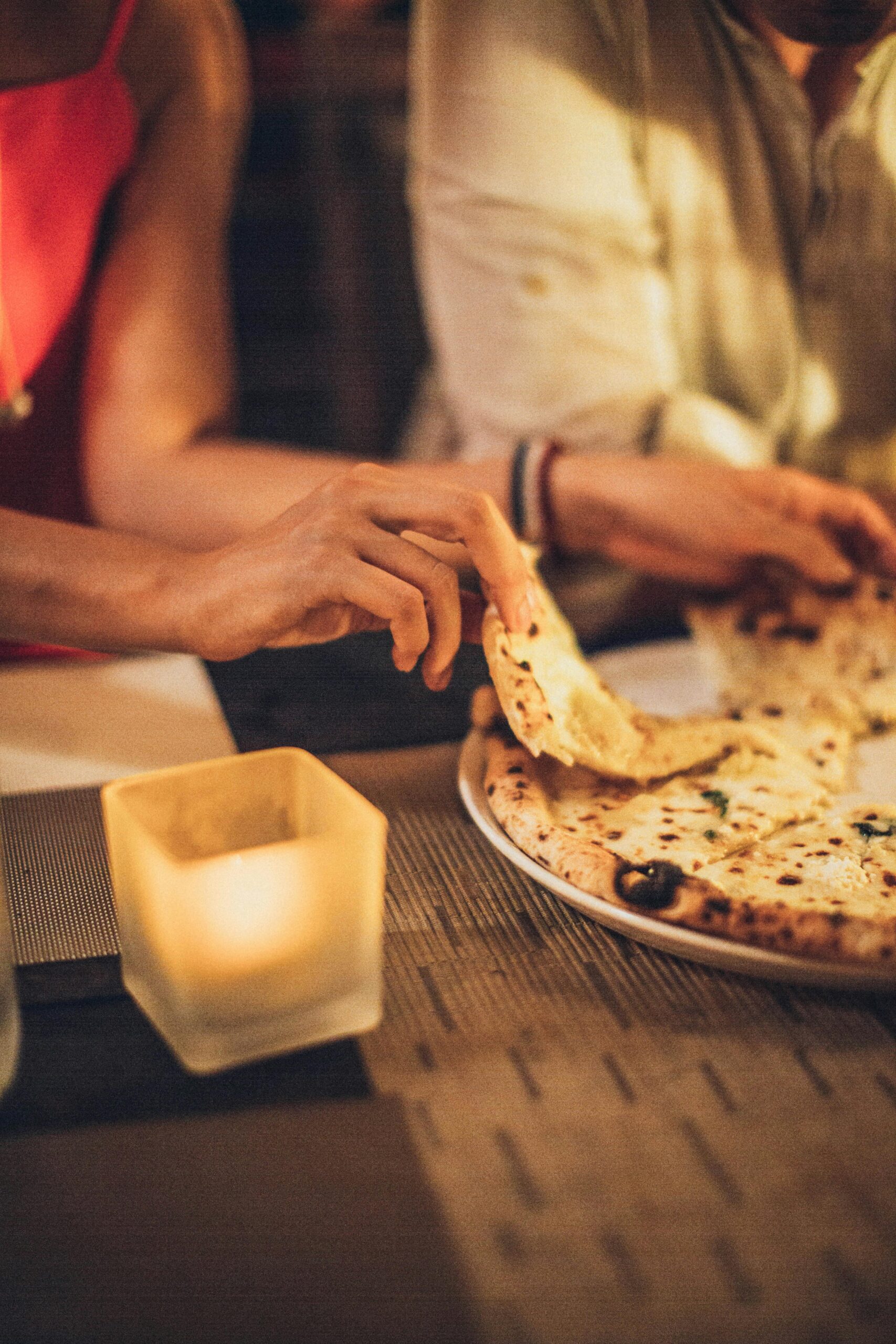 Close-up of a couple enjoying pizza by candlelight in a cozy restaurant setting.
