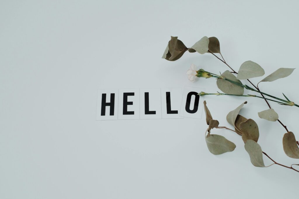 A minimalist flat lay featuring a 'HELLO' note with eucalyptus leaves on a white background.