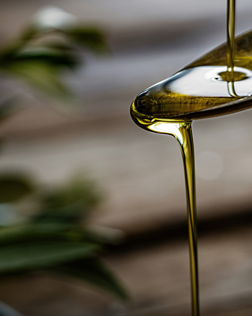 Golden Tuscan extra virgin olive oil pouring from a spoon, with olive leaves softly blurred behind