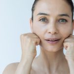 fWoman over 40 doing a face yoga jaw release, resting her knuckles gently along her jawline