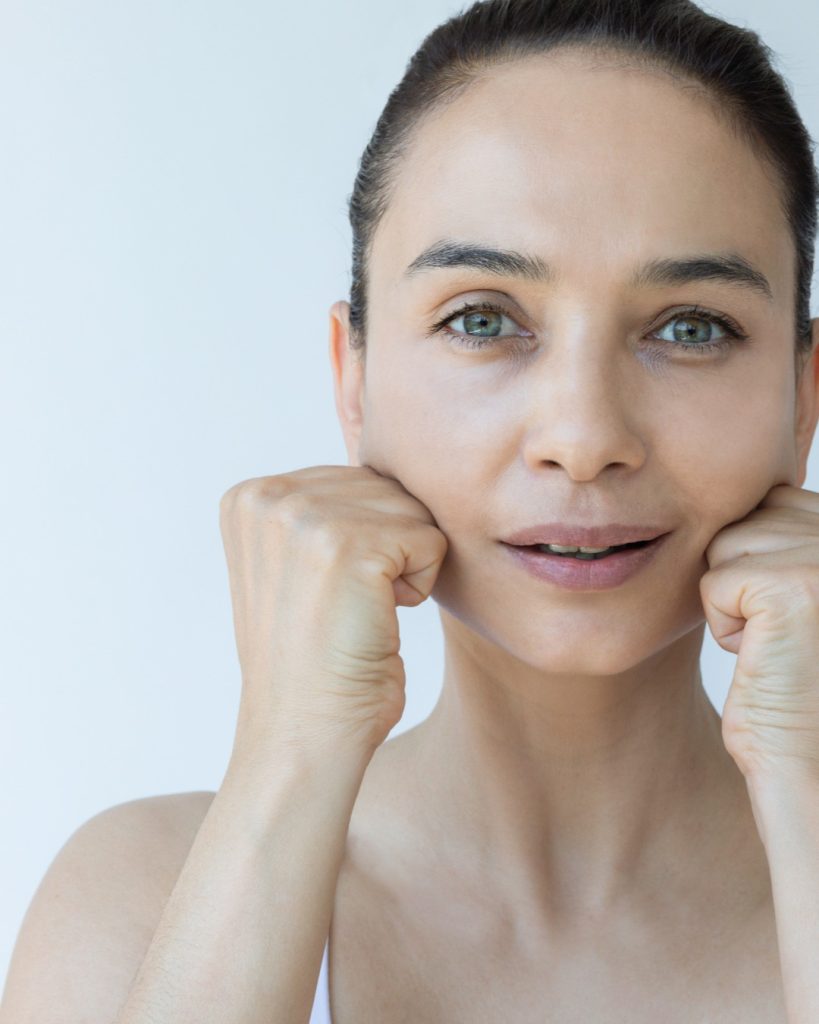 fWoman over 40 doing a face yoga jaw release, resting her knuckles gently along her jawline