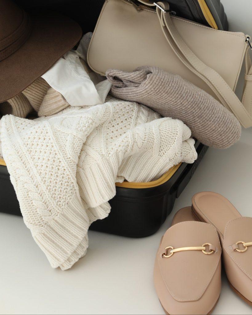Open suitcase packed with cream knitwear, a beige bag and loafers for a wellness retreat in Tuscany